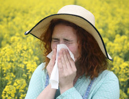 A woman in a field of flowers sneezes into a tissue.