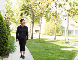 A smiling woman in fitness clothes walks down a sidewalk.