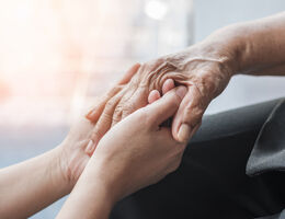 Two hands wrapped around an older person’s hand.