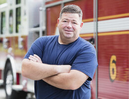A man poses in front of a firetruck.