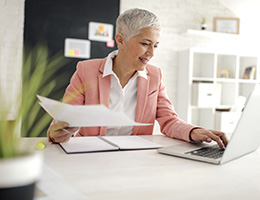 A woman sits at a desk with papers and a laptop computer.