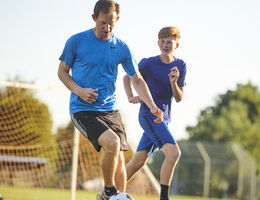 A man and a boy playing soccer on a sunny day.